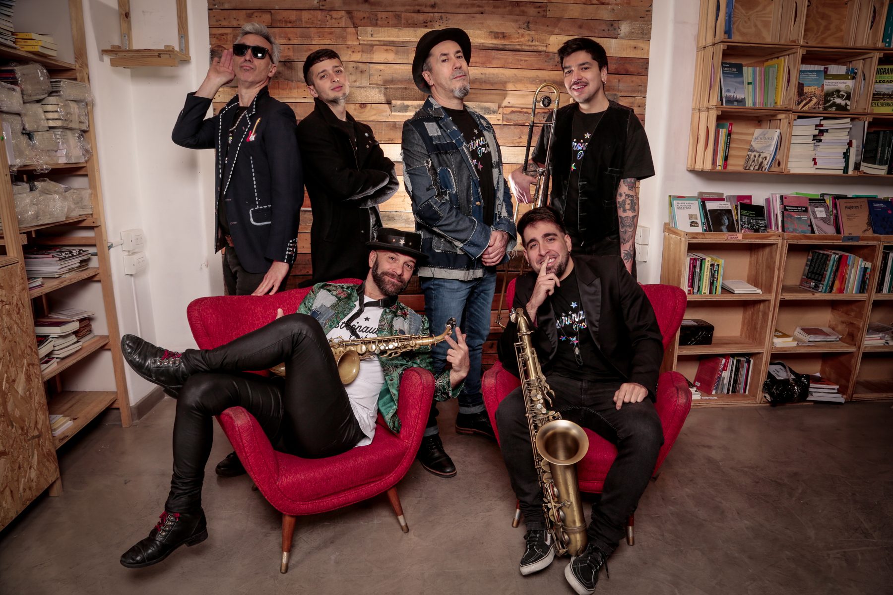 La banda en sillones rojos frente a una pared de madera